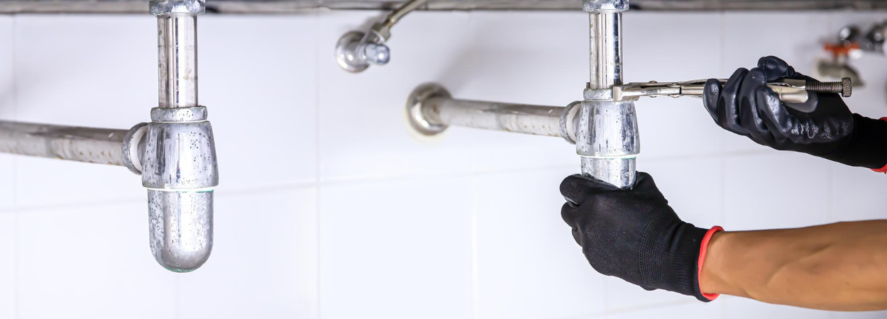 Plumber tightening drain pipe connections under sink – Plumber Pro Dallas